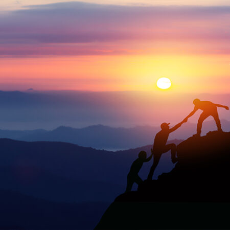 People aiding one another up a mountain at sunset.